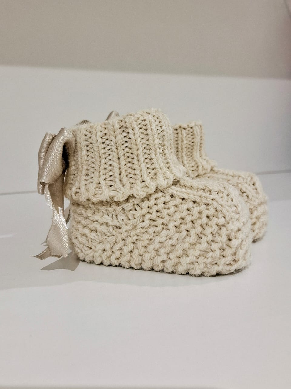 Knitted baby boots adorned with a ribbon at the back.
