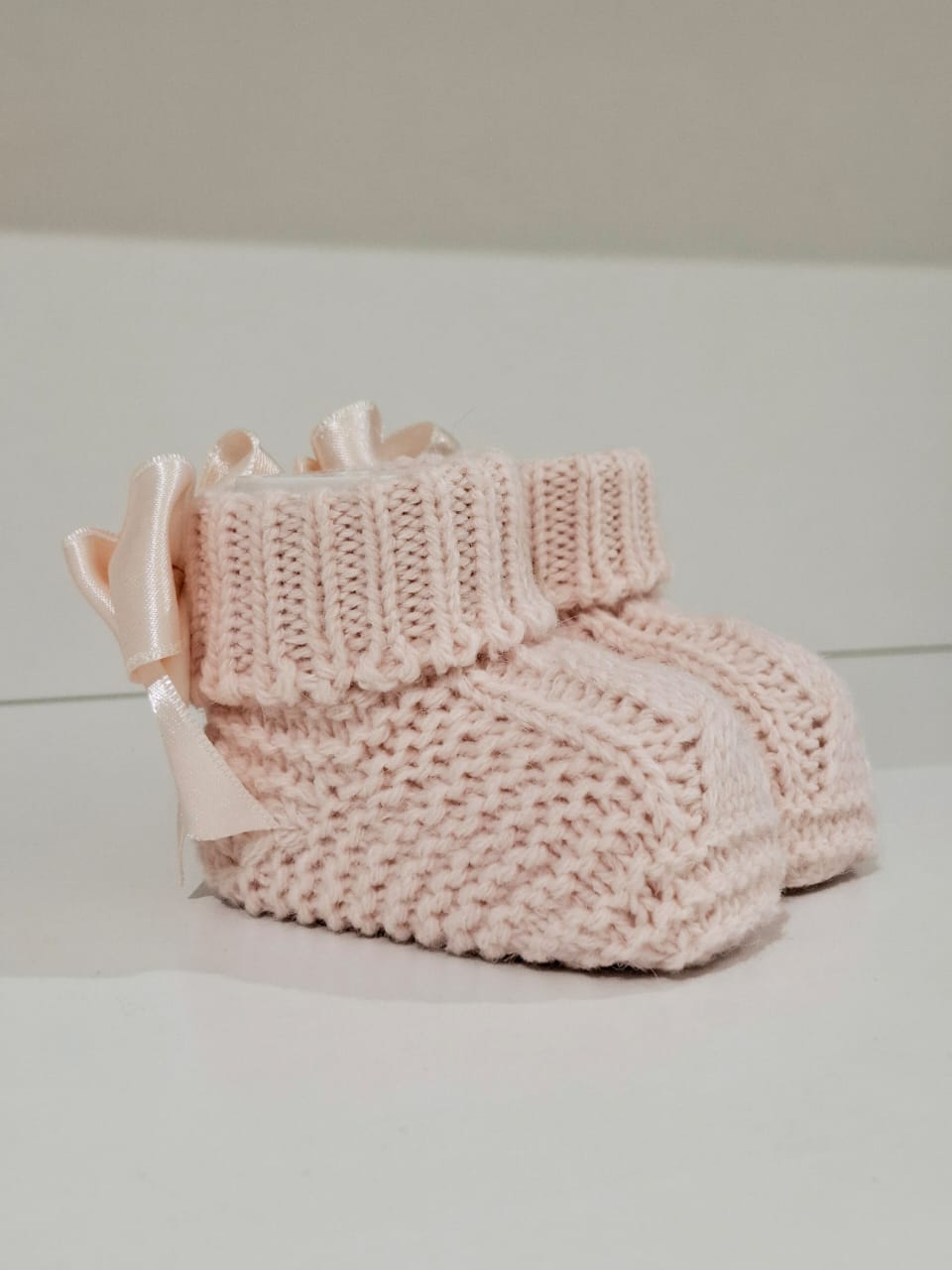 Knitted baby boots adorned with a ribbon at the back.